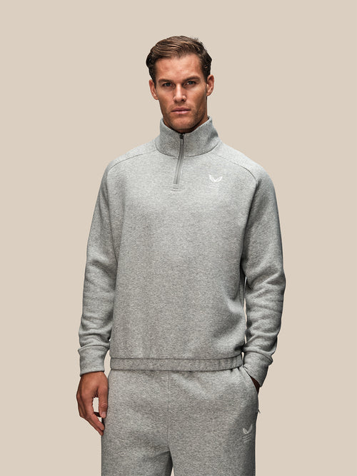 Model in light grey oversized quarter zip sweatshirt with high collar and chest logo