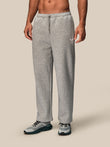 A man wearing light gray heather sweatpants and gray athletic sneakers, shown from the waist down against a plain beige studio background.