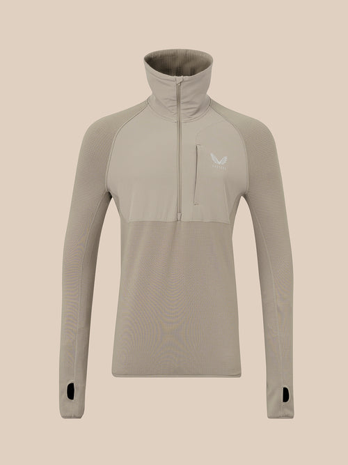 A long-sleeve quarter-zip pullover top in a light taupe-beige color, featuring a high mock neck collar, a vertical zippered chest pocket, and a small white wing logo on the left chest, displayed on a solid beige background.