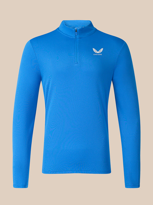 A bright blue long-sleeve quarter-zip pullover top with a small white wing logo and the word 'CASTORE' on the left chest, displayed on a solid beige background.