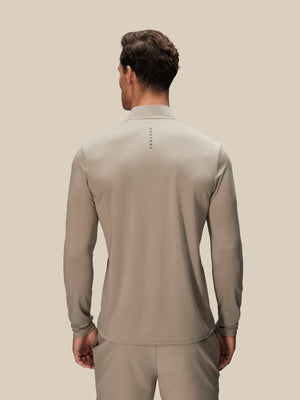 A man viewed from the back wearing a light taupe long-sleeve athletic quarter-zip pullover and matching pants against a solid beige background.