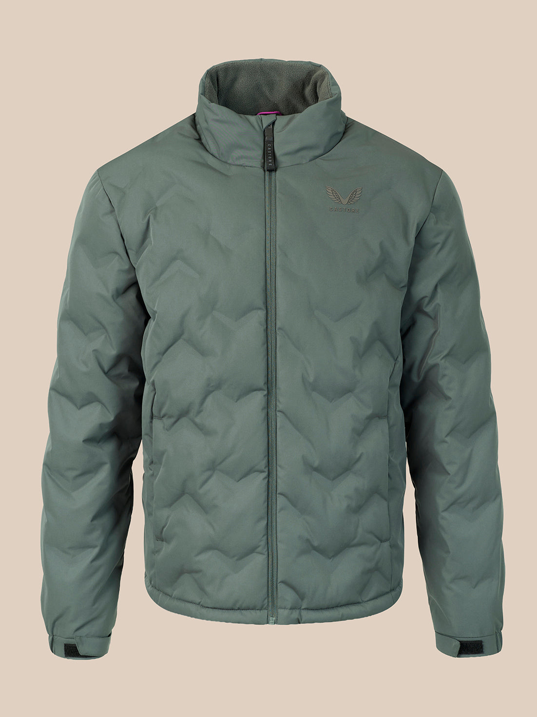 A sage green quilted puffer jacket with a stand-up collar and front zipper, featuring a small embroidered wing logo on the left chest, displayed against a solid beige background.