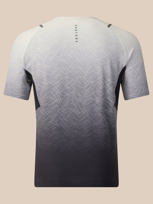 A short-sleeve athletic t-shirt shown from the back, featuring a gradient design that fades from white and light gray at the top to a dark charcoal gray at the bottom. The shirt has a subtle geometric pattern overlay and the brand name 'CASTORE' printed vertically on the upper back, set against a solid beige background.