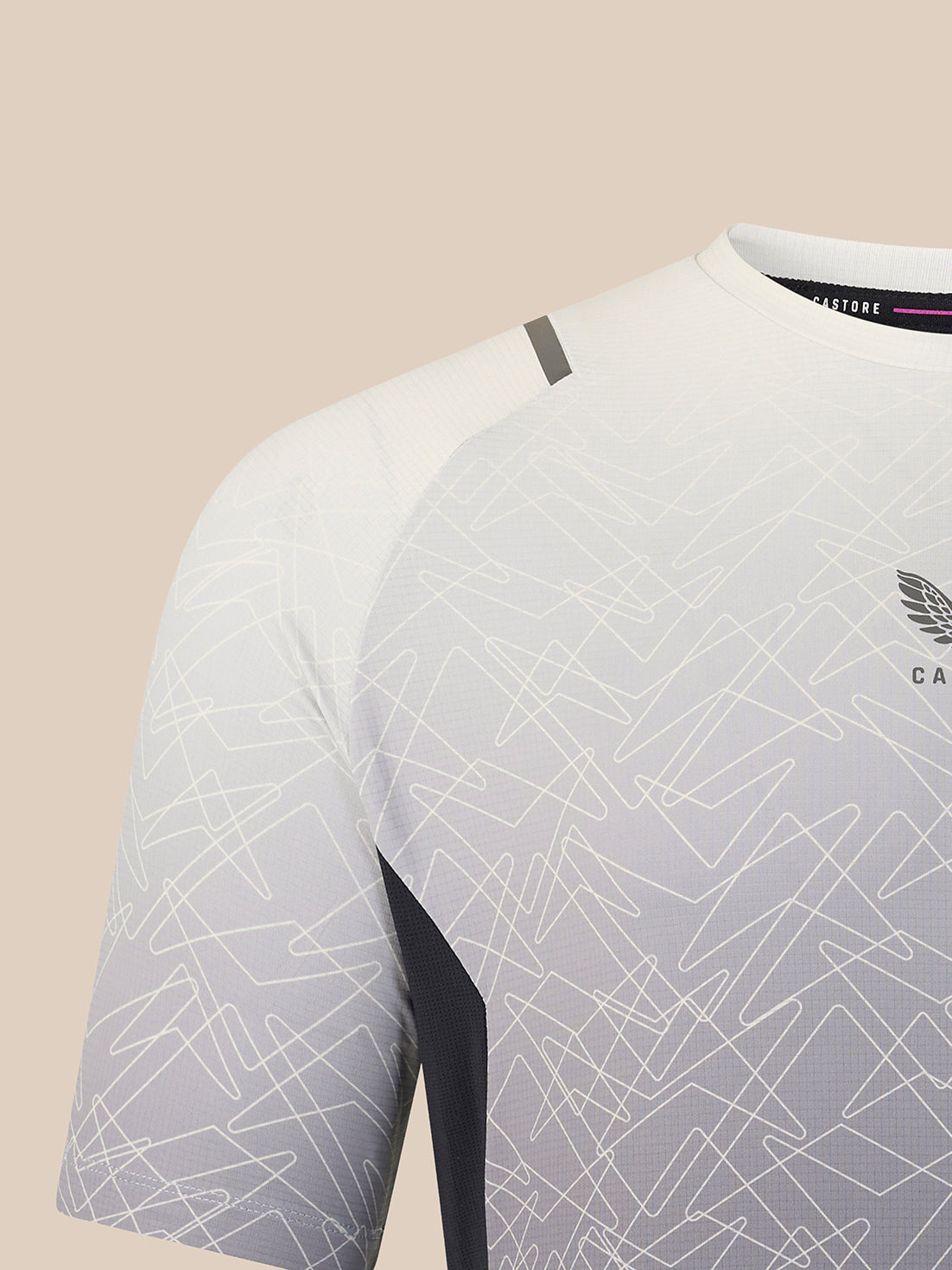 Close-up of a short-sleeve athletic jersey in white and light gray with an allover abstract line pattern, dark side paneling, and a small wing logo on the chest.