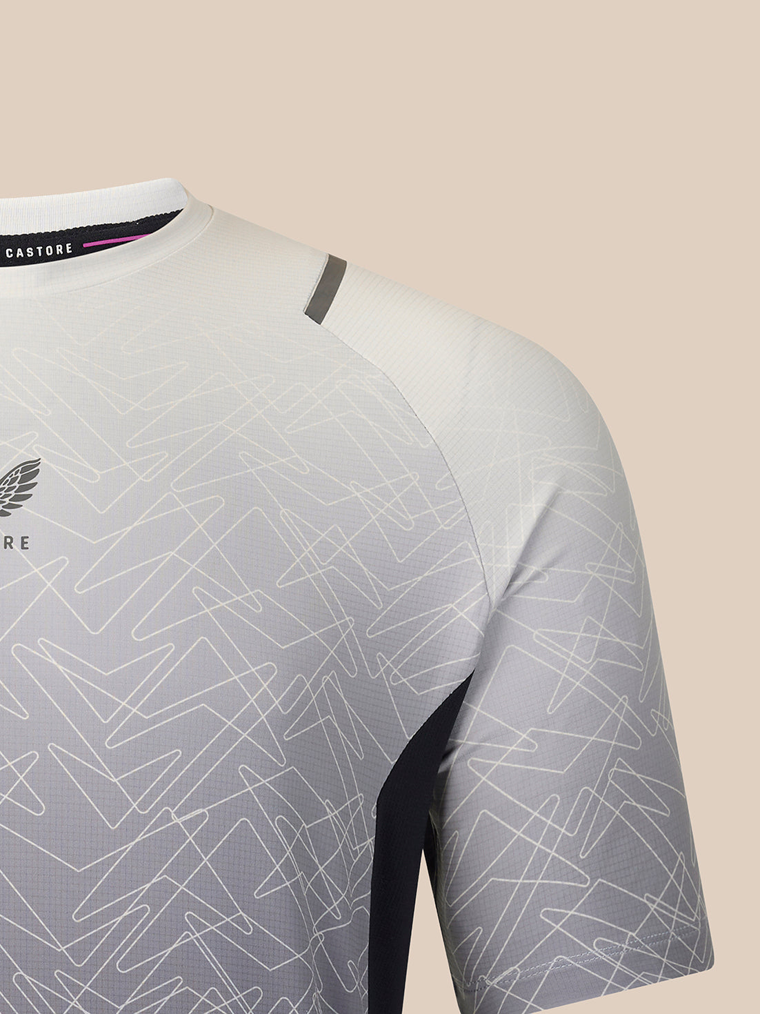 Close-up of a short-sleeve athletic jersey in white and light gray with an abstract line pattern, featuring a dark gray shoulder accent and a black Castore neck label.