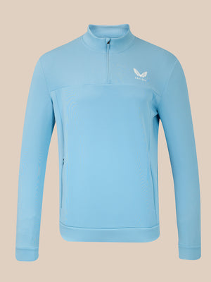 A light blue long-sleeve quarter-zip pullover jacket with a small white wing logo on the left chest, displayed on a solid beige background.