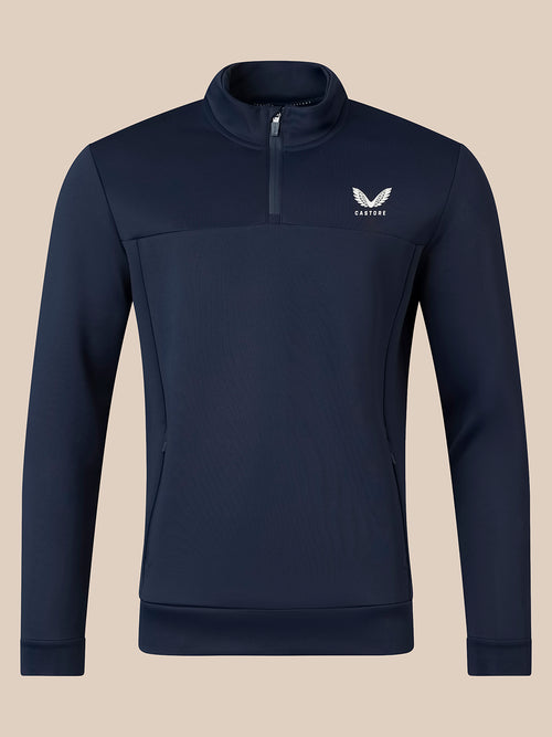 A navy blue long-sleeve quarter-zip pullover sweatshirt with a small white winged logo and the brand name 'castore' on the left chest, displayed against a solid beige background.