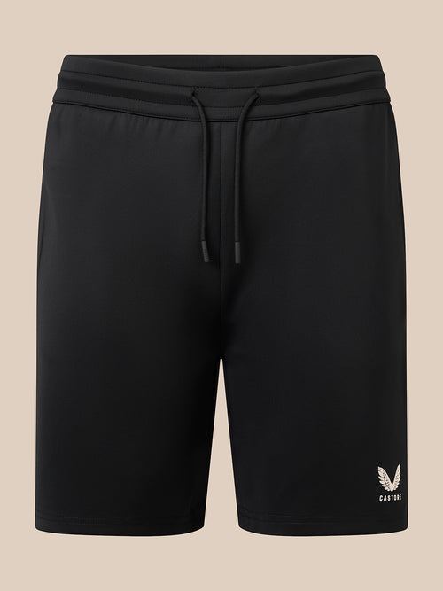 Black athletic shorts with a drawstring waistband and a small white embroidered logo on the lower left leg, shown against a solid beige background.