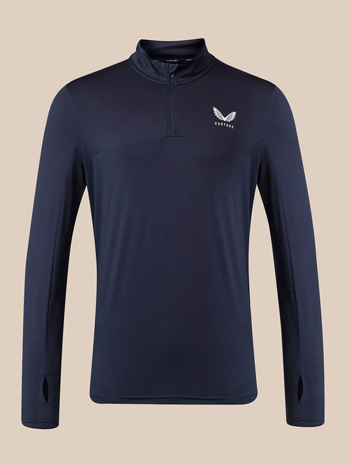 A navy blue long-sleeve quarter-zip athletic pullover with a white wing logo and the word 'Castore' on the left chest, displayed against a solid beige background.