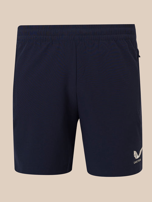 Navy blue athletic shorts with an elastic waistband and a small white embroidered logo on the lower left leg, shown against a solid beige background.