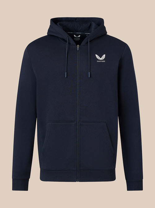 A navy blue zip-up hoodie with a white embroidered winged logo on the left chest, displayed on a solid beige background.