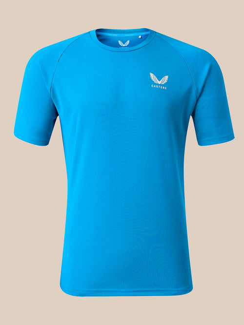 A bright blue short-sleeve athletic t-shirt with a small white winged logo and the brand name 'CASTORE' printed on the left chest, displayed on a solid beige background.