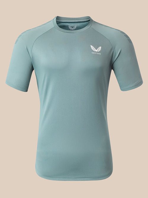 A light blue athletic short-sleeve t-shirt with a white wing logo and the brand name 'Castore' printed on the left chest, displayed on a neutral beige background.