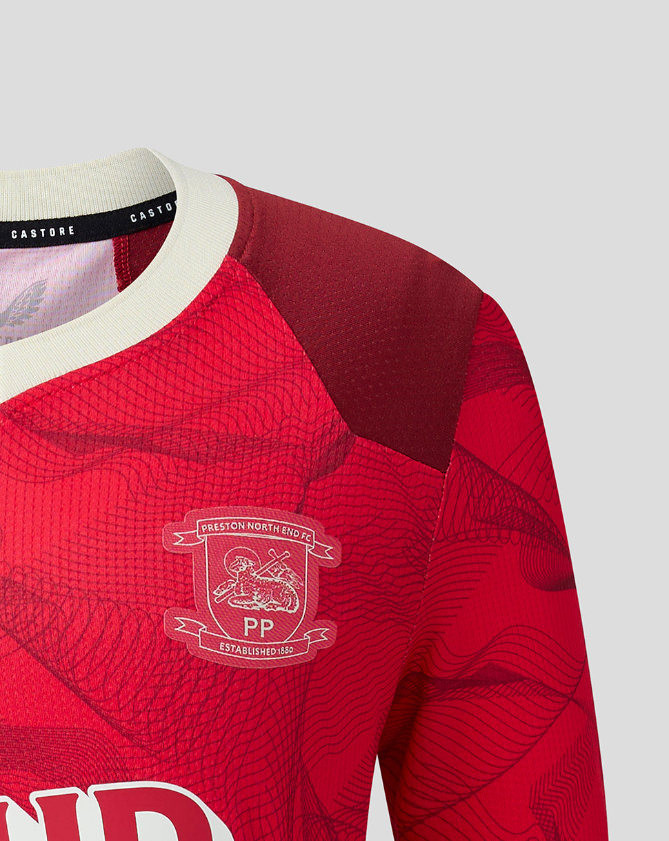 Close-up of a red long-sleeve sports jersey with a subtle wavy pattern, featuring a white collar, a dark red shoulder yoke, and the Preston North End FC crest on the left chest.