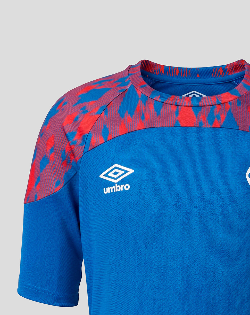 Close-up of a blue short-sleeve athletic jersey with red abstract patterned shoulder panels and a white Umbro logo on the chest, shown against a light gray background.