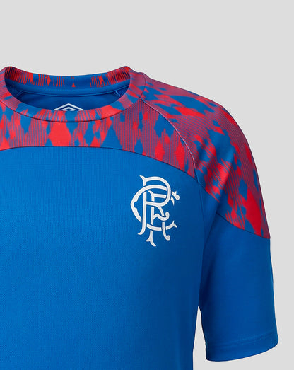 A close-up of a short-sleeve athletic jersey in royal blue with a red and blue patterned yoke and shoulder area, featuring a white Rangers FC crest on the chest.