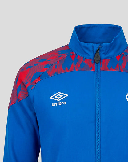 A close-up of a blue and red patterned athletic jacket by Umbro, featuring a white embroidered logo on the chest, a high collar, and a front zipper, set against a plain light gray background.