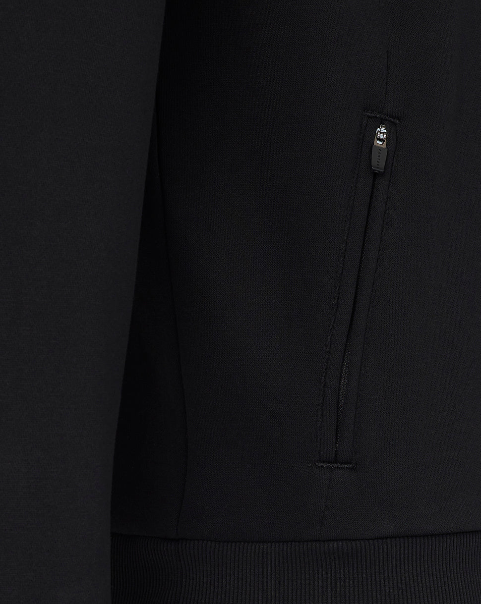Close-up of a black hoodie with a brand logo on the chest pocket against a dark background.
