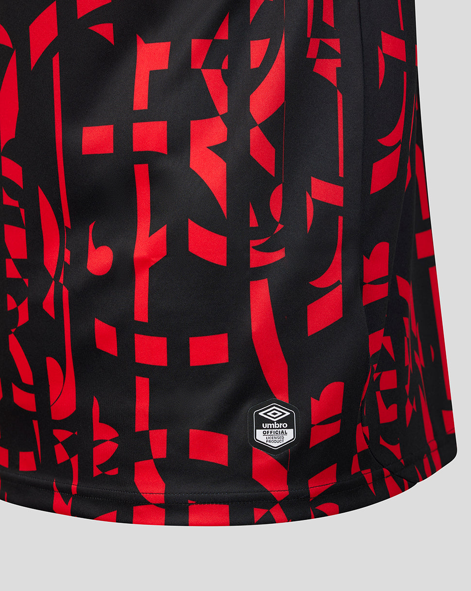 Close-up of a black athletic jersey or shorts with a bold red abstract geometric pattern and a small Umbro logo patch near the lower hem, shown on a light gray background.