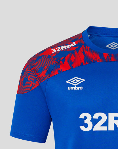 Close-up of a blue soccer jersey with a red and blue patterned shoulder panel, white Umbro logo, and white '32Red' text on a light gray background.