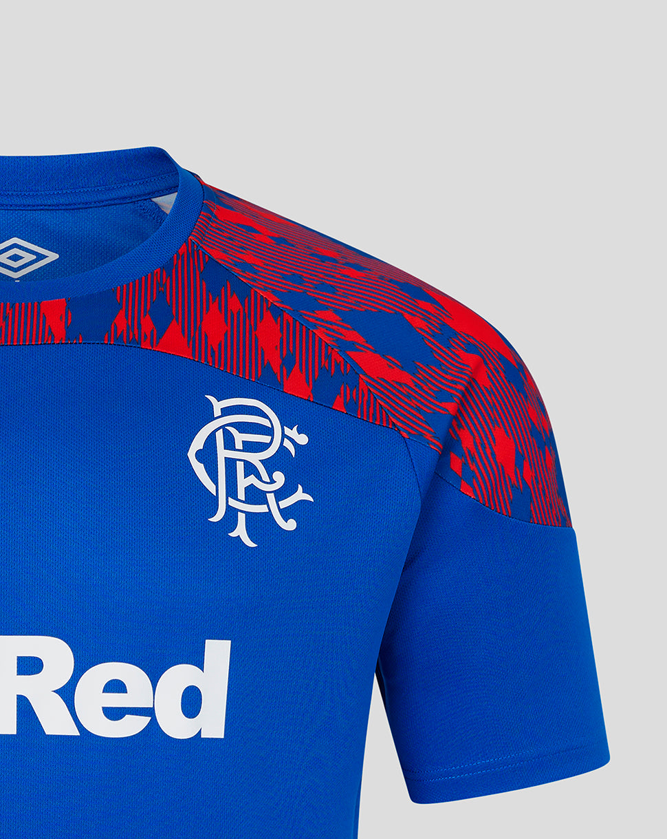 Close-up of a blue short-sleeve soccer jersey with red abstract patterned shoulder panels, a white Rangers FC crest on the chest, and part of a white sponsor logo reading 'Red' on a light gray background.