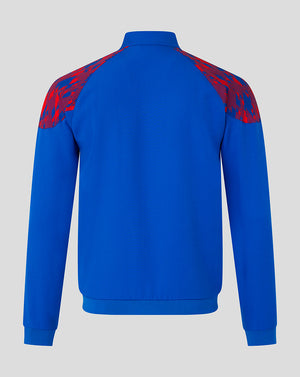 A royal blue long-sleeve track jacket shown from the back, featuring red and blue abstract patterned shoulder yokes, set against a solid light gray background.
