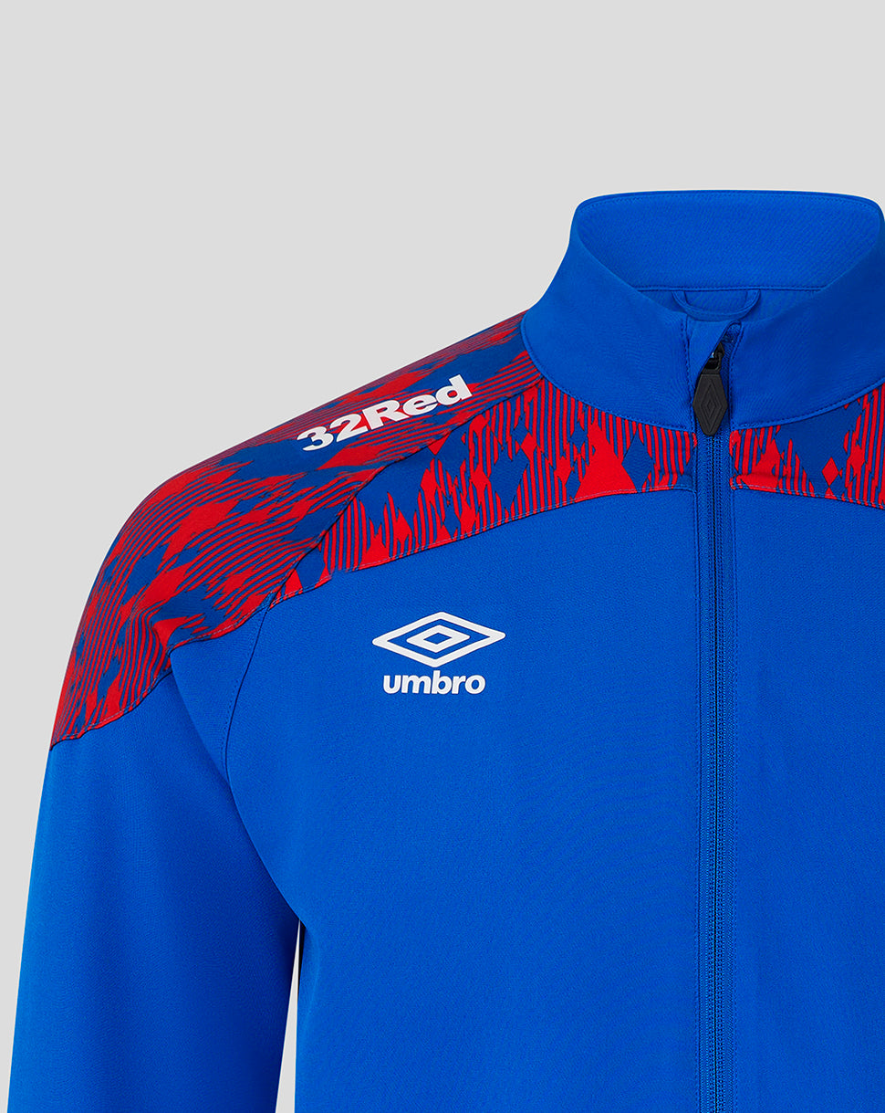 A close-up of a blue and red patterned athletic jacket by Umbro, featuring a white embroidered logo on the chest and '32Red' text on the shoulder, set against a light gray background.