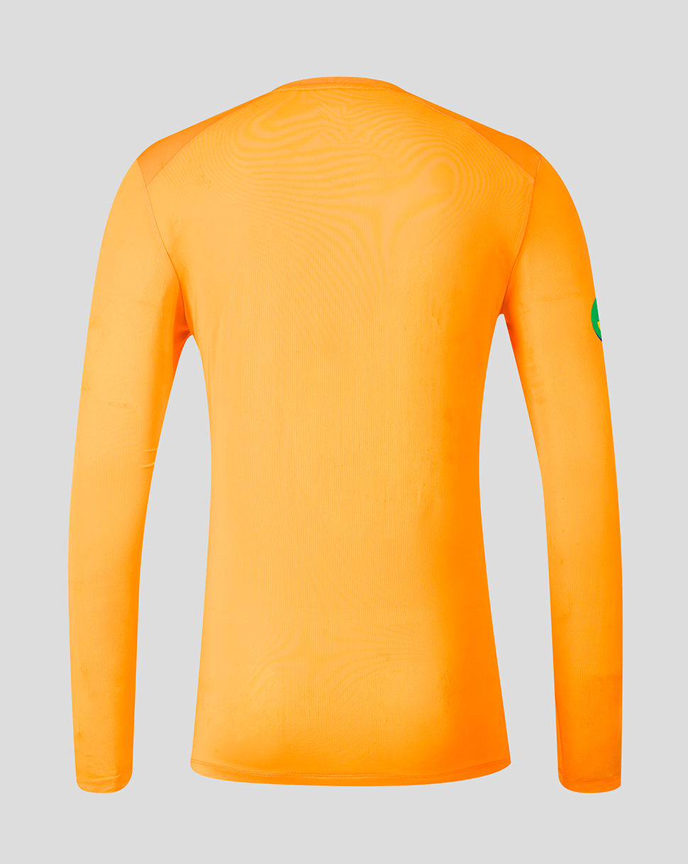 A bright orange long-sleeve athletic shirt shown from the back, featuring a subtle wavy texture across the upper back and a small green patch on the right sleeve, set against a solid light gray background.
