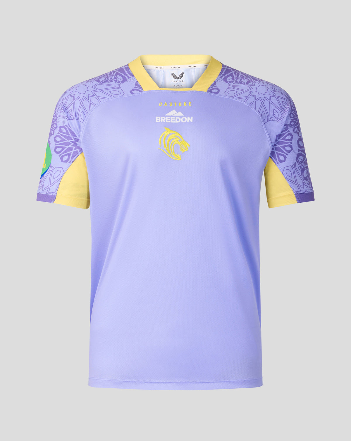 A short-sleeve soccer jersey in light purple with yellow sleeves and collar trim, featuring a purple mandala pattern on the shoulders and a yellow lion crest on the chest.
