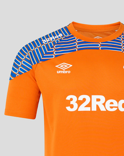 Close-up of an orange football jersey with blue patterned shoulder panels, a white Umbro logo, and a large white 32Recor sponsor logo on a light gray background.