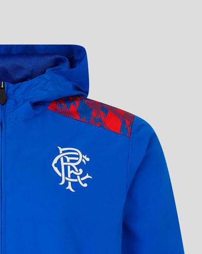 Close-up of a royal blue hooded jacket with a red patterned shoulder panel and a white stylized chest logo, shown against a light gray background.