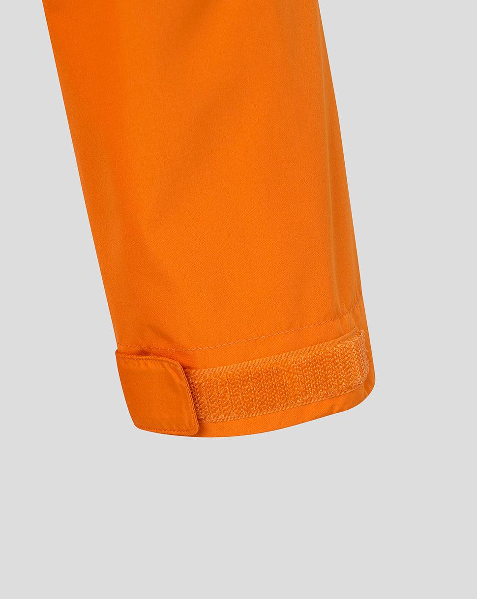 Close-up of an orange garment sleeve or leg section with a hook-and-loop cuff closure, shown against a light gray background.