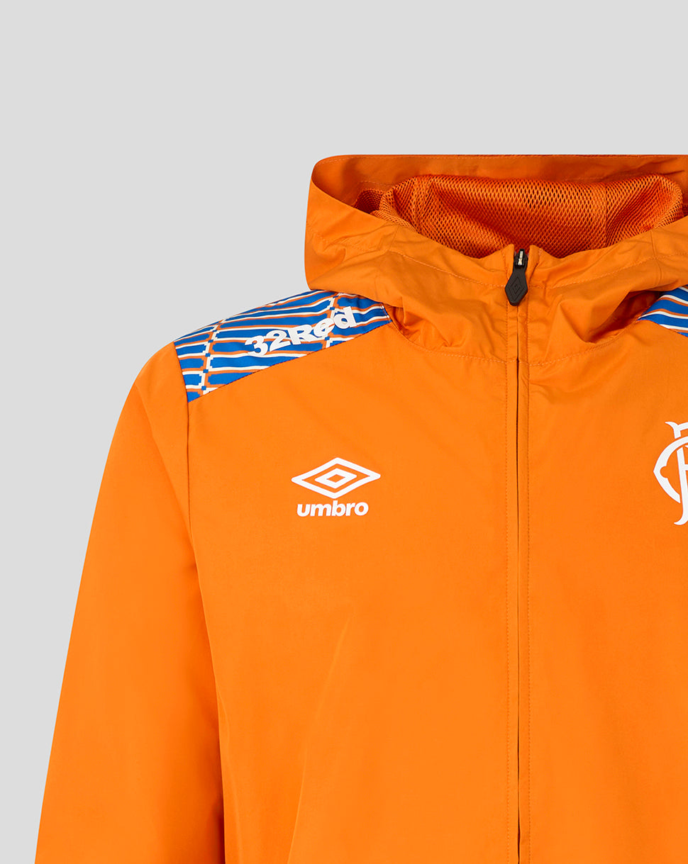 Close-up of an orange hooded jacket with a white Umbro logo on the chest and blue patterned shoulder detailing, shown against a light gray background.