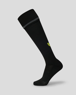 A single black knee-high athletic sock with a small yellow logo on the side and a gray ribbed band at the top cuff, shown against a solid light gray background.
