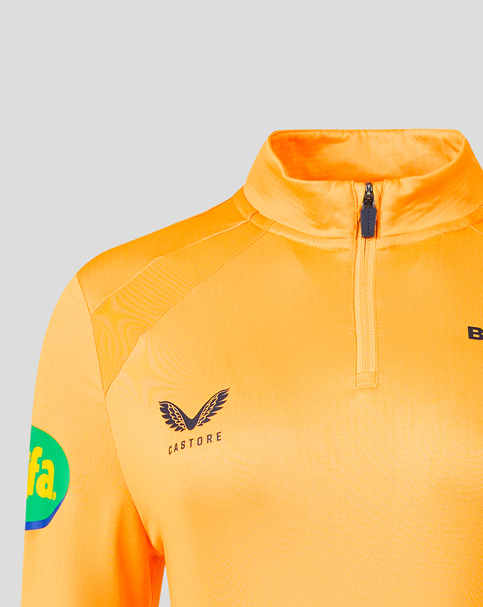 Close-up of a bright orange athletic quarter-zip pullover with a stand collar, featuring a black Castore wing logo on the chest and a green circular patch on the sleeve, set against a light gray background.