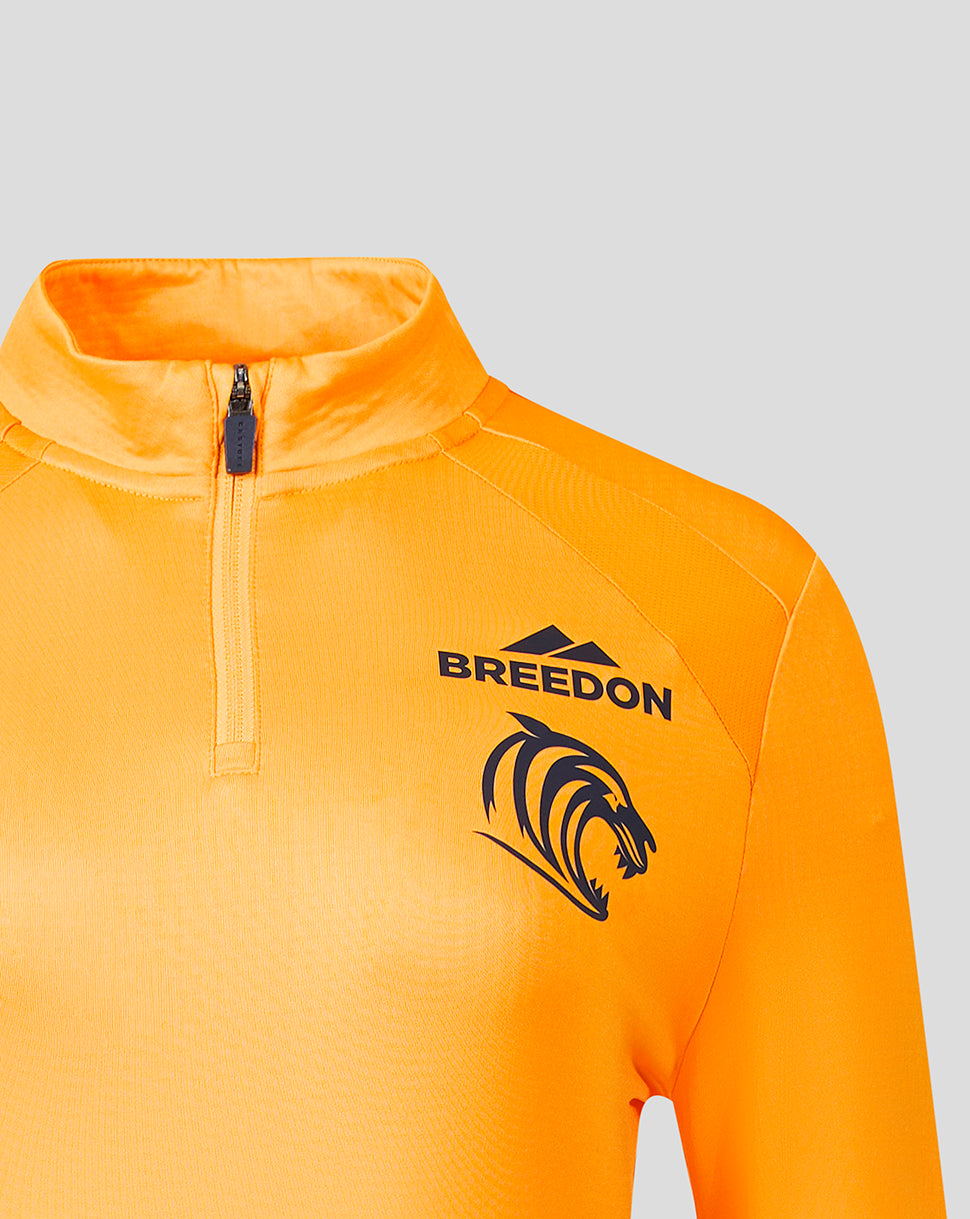 Close-up of a bright orange athletic quarter-zip top with a black 'BREEDON' wordmark and lion head logo on the chest, shown against a light gray background.