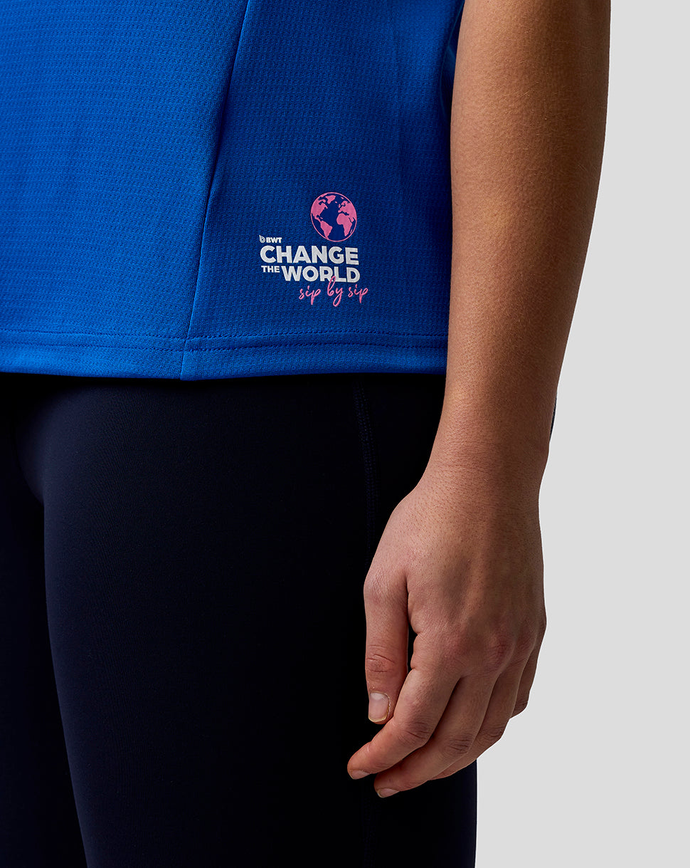 Blue shirt with a logo and text on a person wearing black pants against a light gray background