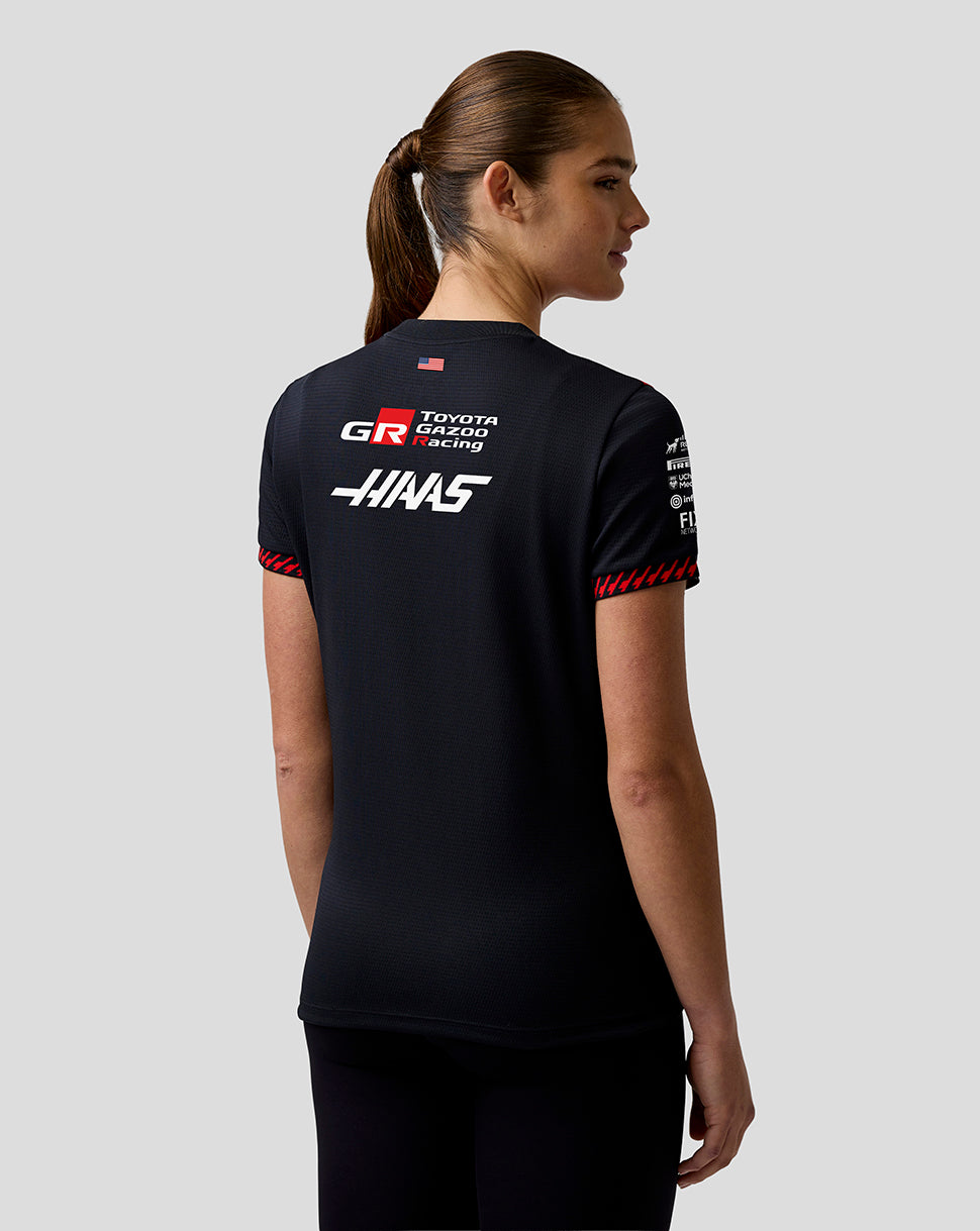 Person wearing a black t-shirt with racing team logos on a light gray background