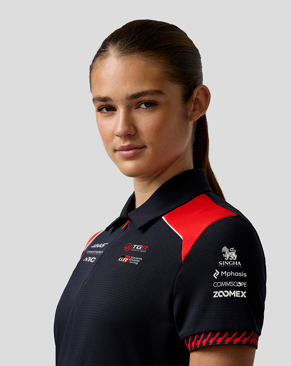 Woman wearing a black and red polo shirt with various logos on a light gray background