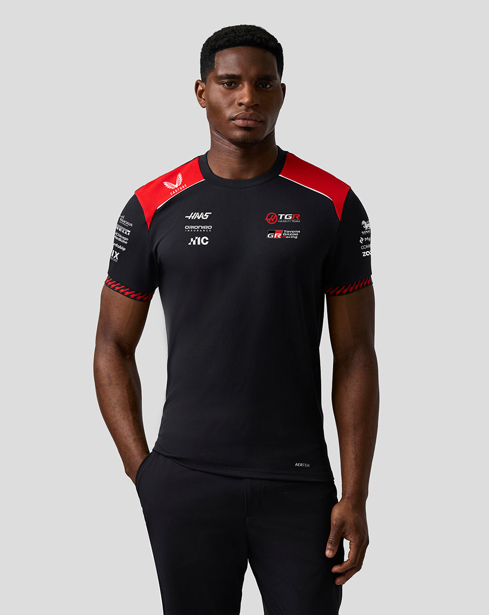 Person wearing a black and red sports outfit with various logos on a gray background