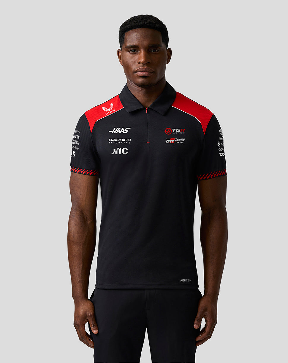 Person wearing a black and red polo shirt with various logos on a gray background