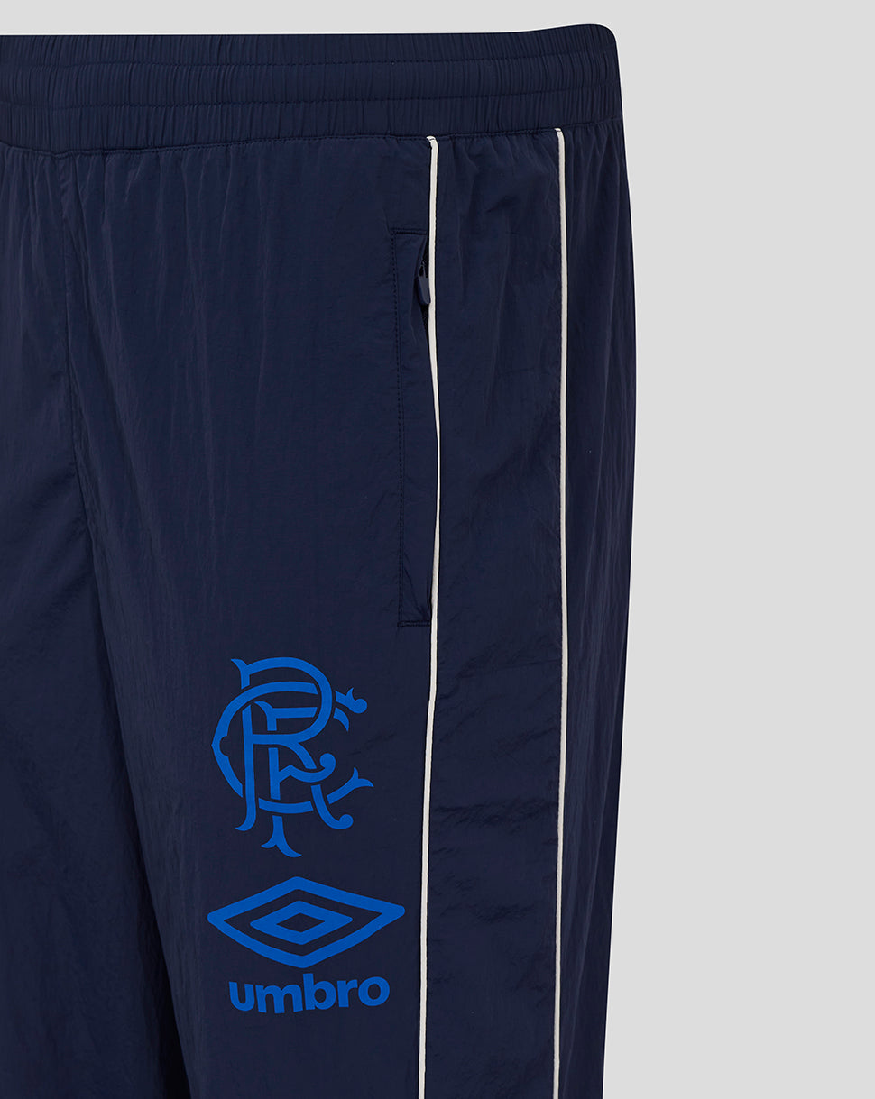 Navy travel pant leg close-up with white piping concealed zip pocket and visible club crest with Umbro logo