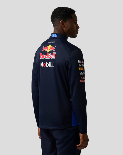 Person wearing a dark blue tracksuit with Red Bull and Mobil logos on the back against a light gray background