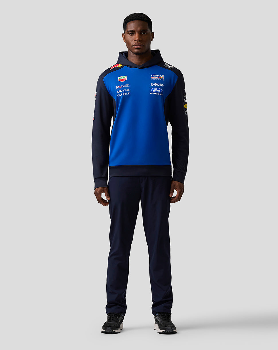 Person wearing a blue and black tracksuit with various logos on a white background