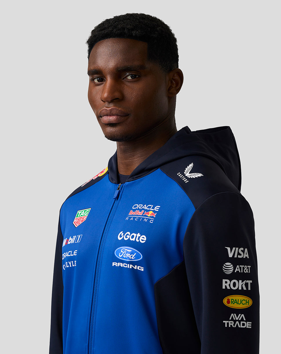 Person wearing a blue and black racing jacket with various sponsor logos on a gray background