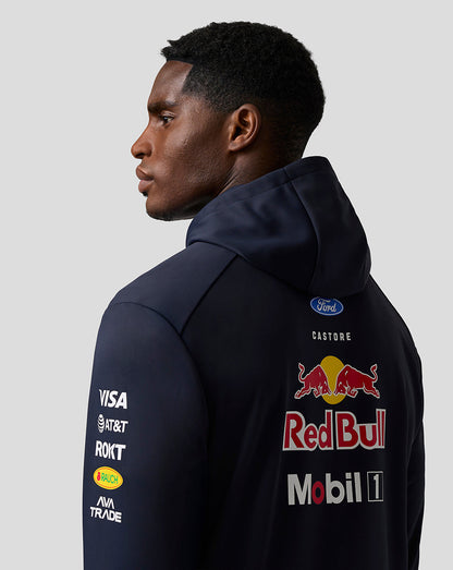 Person wearing a dark blue jacket with various logos on a light gray background
