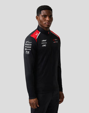 Person wearing a black tracksuit with various logos on a gray background