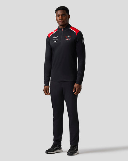 Person wearing a black tracksuit with red accents on a gray background