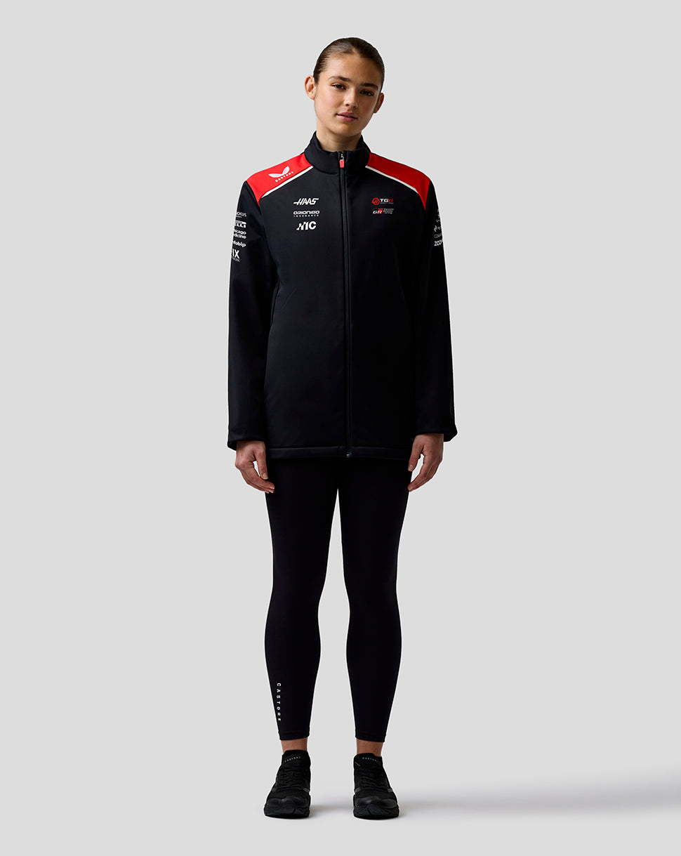 Person wearing a black jacket with red accents and logos on a light gray background