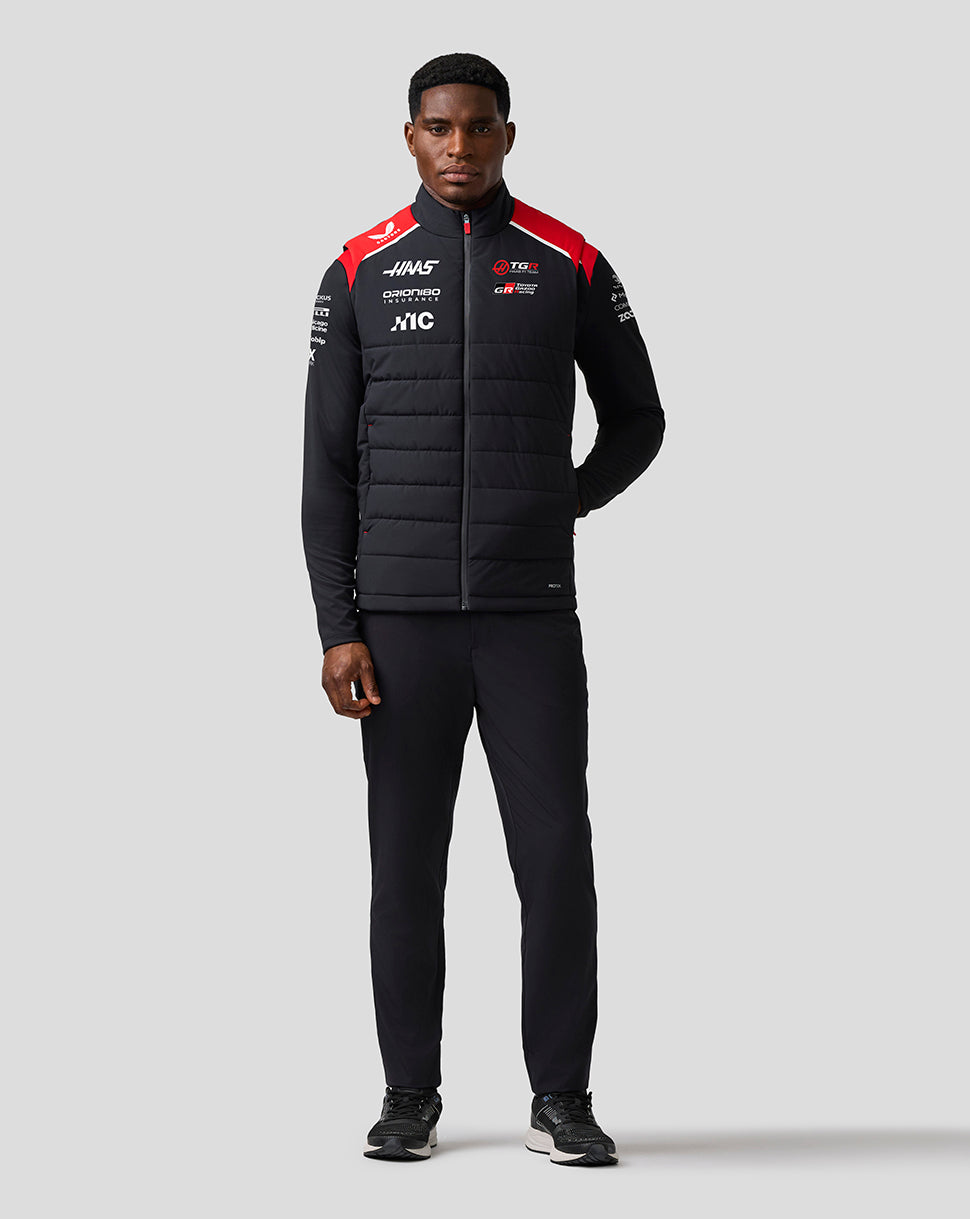 Person wearing a black puffer jacket with red and white accents on a gray background
